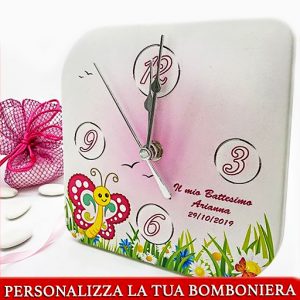 Bomboniera orologio battesimo, realizzato con supporto in legno rivestito in ecopelle con stampa colorata di un prato fiorito con una farfalla e sfondo rosa, ideale per l'evento di una femminuccia.