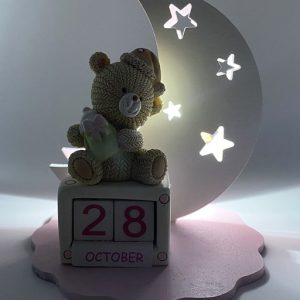Lampada orsetto dondolo con datario rosa realizzato in legno color rosa e bianco a forma di luna traforata con piccole stelle.