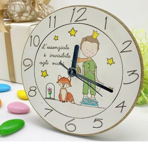 Orologio piccolo principe realizzato in legno, base in rovere e una superficie bianca che ospita una deliziosa raffigurazione della volpe e del Piccolo Principe indossanti una sciarpa e una corona.