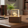 Cubo laurea in cristallo con base in legno. La bomboniera è realizzata in vetro, alla base una luce led rende atmosfera magica